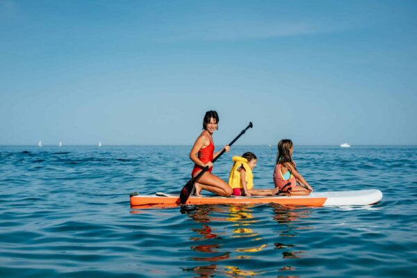 Mother with two daughters stand up on a paddle board. At sea, calm.